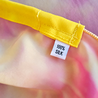 Close-up of the 100% silk label beneath the yellow rod pocket on GOOD SHEPHERD flags, with soft fuchsia, purple, and yellow silk.